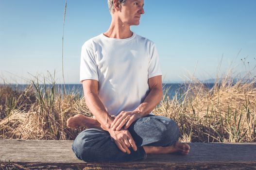 Man sitting in a relaxed yoga pose at the beach.