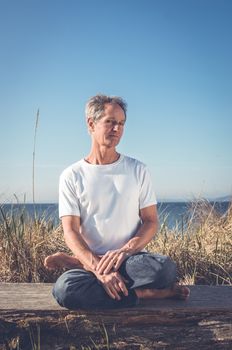 Man sitting in a relaxed yoga pose at the beach.