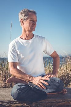 Man sitting in a relaxed yoga pose at the beach.