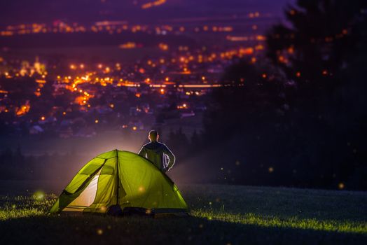 Countryside Camping with Scenic City View Down the Valley. Illuminated Cityscape at Night and the Camper with Illuminated Tent. Countryside Getaway.