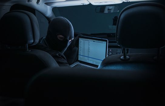 Hacking Inner Car Systems. Car Robber with Laptop Trying to Hack Modern Car System While Seating Inside the Car. 