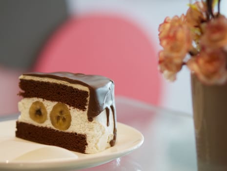 Delicious banana chocolate cake on white plate on table in restaurant.