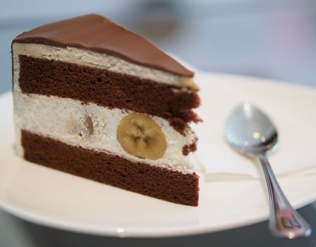 Delicious banana chocolate cake on white plate on table in restaurant.
