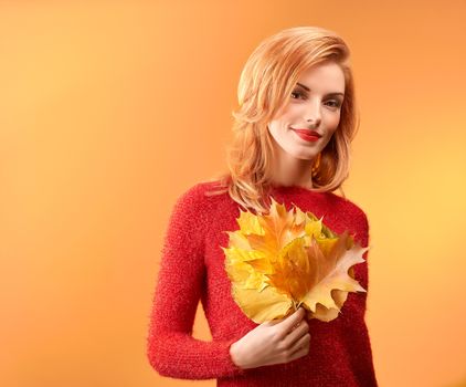 Beauty portrait redhead young model woman, autumn leafs in hands. Attractive happy playful girl in stylish red sweater smiling, people. Retro vintage, creative toned.Orange yellow background,copyspace