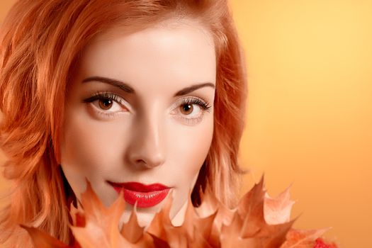 Beauty portrait redhead young woman with autumn leafs smiling. Attractive happy girl dreams, romantic. People face closeup, makeup. Retro, vintage, creative toned, orange yellow background, copyspace