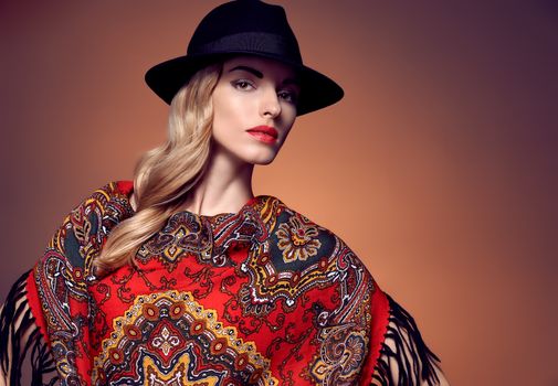 Fashion beauty woman in stylish hat, colored cashmere shawl. Autumn winter model blond girl with long blonde wavy hair, ethnic pattern headscarf. Unusual creative attractive people. Retro Vintage