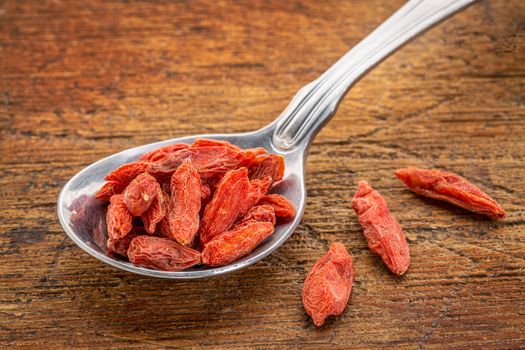 tablespoon of dried goji berries against rustic, scratched wood surface