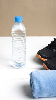 fitness equipment:blue towel,drinking water and running shoes on white wood table