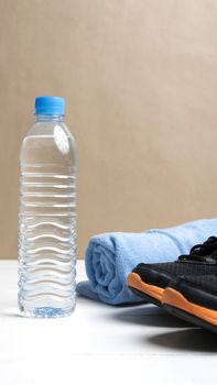 fitness equipment:blue towel,drinking water and running shoes on white wood table