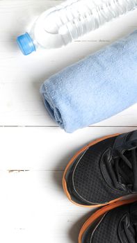 fitness equipment:blue towel,drinking water and running shoes on white wood table