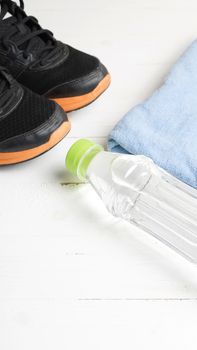 fitness equipment:blue towel,drinking water and running shoes on white wood table