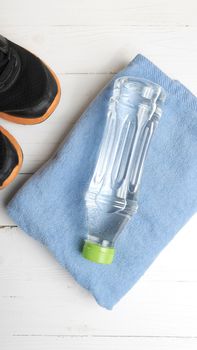 fitness equipment:blue towel,drinking water and running shoes on white wood table