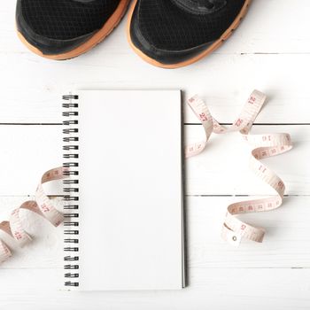 running shoes with notebook and measuring tape on white wood table