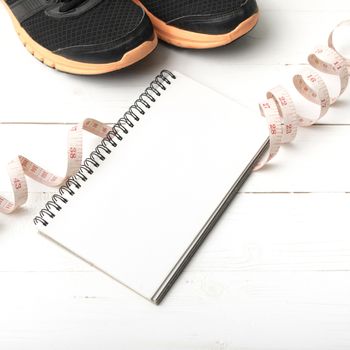 running shoes with notebook and measuring tape on white wood table