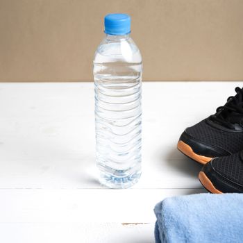 fitness equipment:blue towel,drinking water and running shoes on white wood table