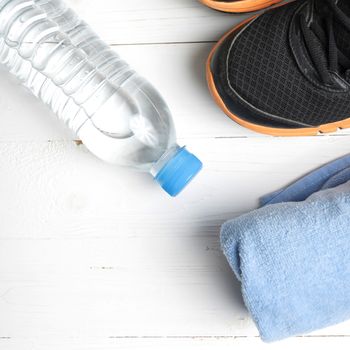 fitness equipment:blue towel,drinking water and running shoes on white wood table