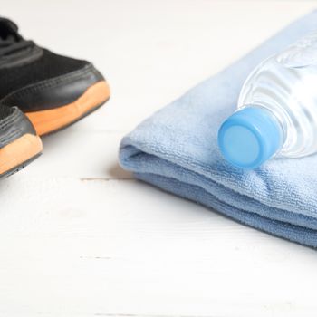 fitness equipment:blue towel,drinking water and running shoes on white wood table