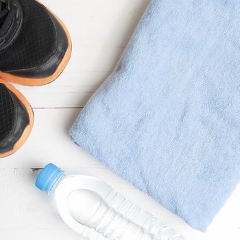 fitness equipment:blue towel,drinking water and running shoes on white wood table