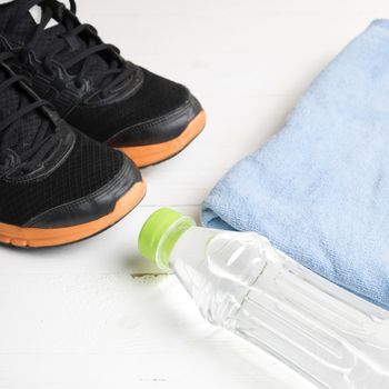 fitness equipment:blue towel,drinking water and running shoes on white wood table