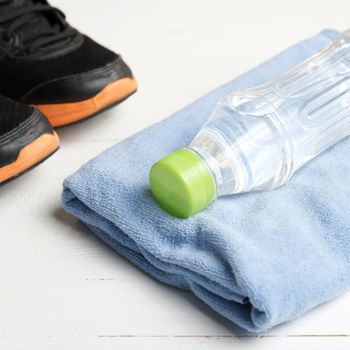 fitness equipment:blue towel,drinking water and running shoes on white wood table