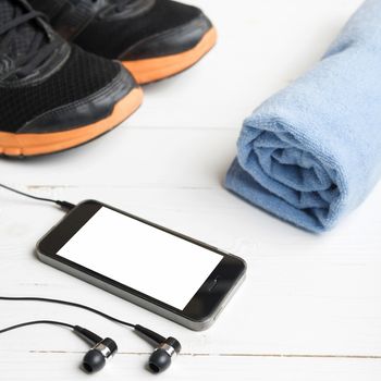 fitness equipment:running shoes,blue towel and smart phone on white wood table