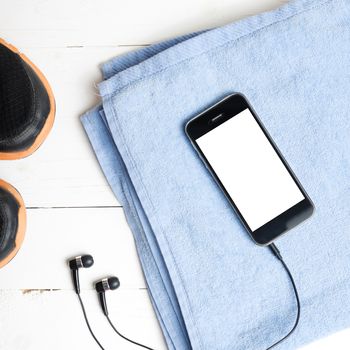 fitness equipment:running shoes,blue towel and smart phone on white wood table