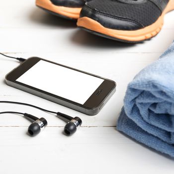 fitness equipment:running shoes,blue towel and smart phone on white wood table