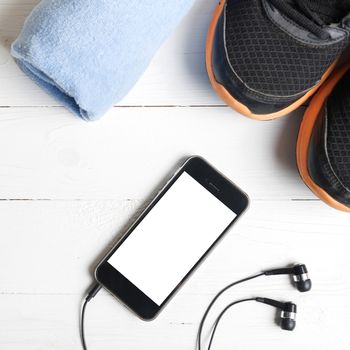 fitness equipment:running shoes,blue towel and smart phone on white wood table