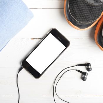 fitness equipment:running shoes,blue towel and smart phone on white wood table