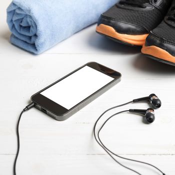 fitness equipment:running shoes,blue towel and smart phone on white wood table