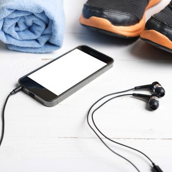 fitness equipment:running shoes,blue towel and smart phone on white wood table