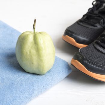 fitness equipment : running shoes,blue towel and guava fruit on white wood table