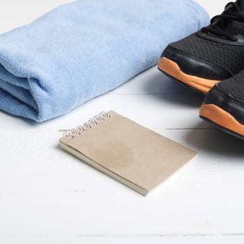 fitness equipment : running shoes,blue towel and notepad on white wood table