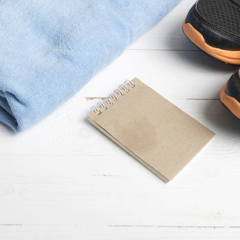 fitness equipment : running shoes,blue towel and notepad on white wood table