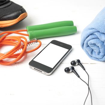 fitness equipment : running shoes,towel,jumping rope and phone on white wood table