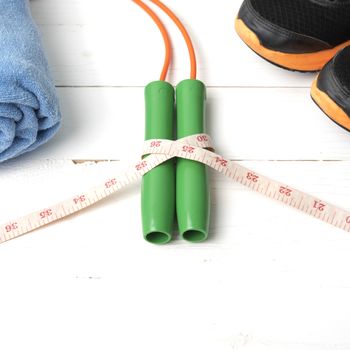 fitness equipment : running shoes,towel,jumping rope and measuring tape on white wood table
