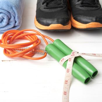 fitness equipment : running shoes,towel,jumping rope and measuring tape on white wood table