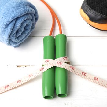 fitness equipment : running shoes,towel,jumping rope and measuring tape on white wood table