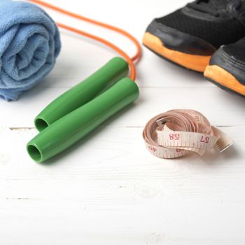fitness equipment : running shoes,towel,jumping rope and measuring tape on white wood table