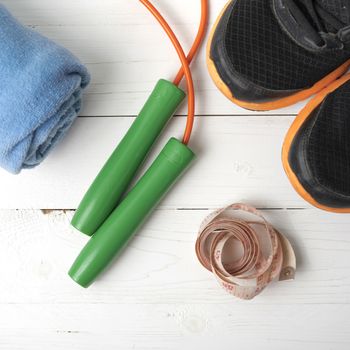 fitness equipment : running shoes,towel,jumping rope and measuring tape on white wood table