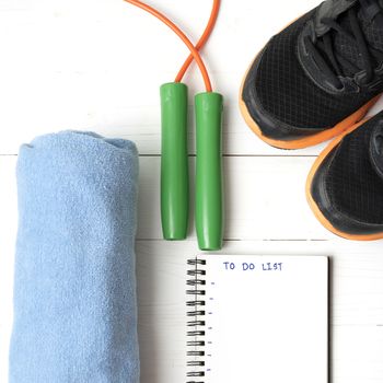 fitness equipment : running shoes,towel,jumping rope and notebook write to do list on white wood table
