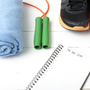 fitness equipment : running shoes,towel,jumping rope and notebook write to do list on white wood table