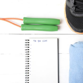 fitness equipment : running shoes,towel,jumping rope and notebook write to do list on white wood table