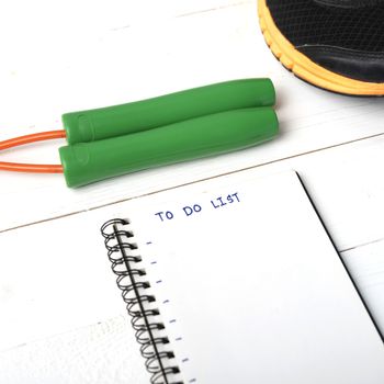 fitness equipment : running shoes,jumping rope and notebook write to do list on white wood table