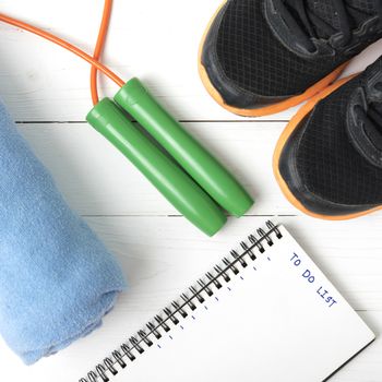 fitness equipment : running shoes,towel,jumping rope and notebook write to do list on white wood table