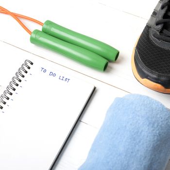 fitness equipment : running shoes,towel,jumping rope and notebook write to do list on white wood table