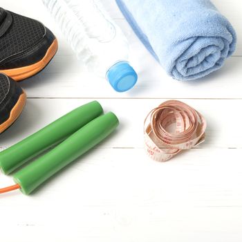 fitness equipment : running shoes,towel,jumping rope,water bottle and measuring tape on white wood table
