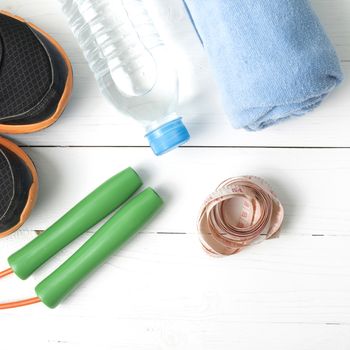 fitness equipment : running shoes,towel,jumping rope,water bottle and measuring tape on white wood table