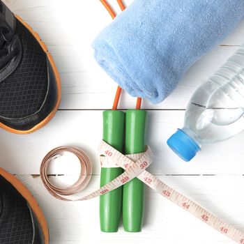 fitness equipment : running shoes,towel,jumping rope,water bottle and measuring tape on white wood table