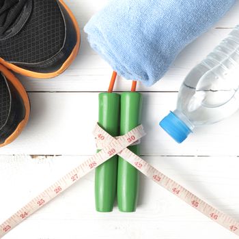 fitness equipment : running shoes,towel,jumping rope,water bottle and measuring tape on white wood table